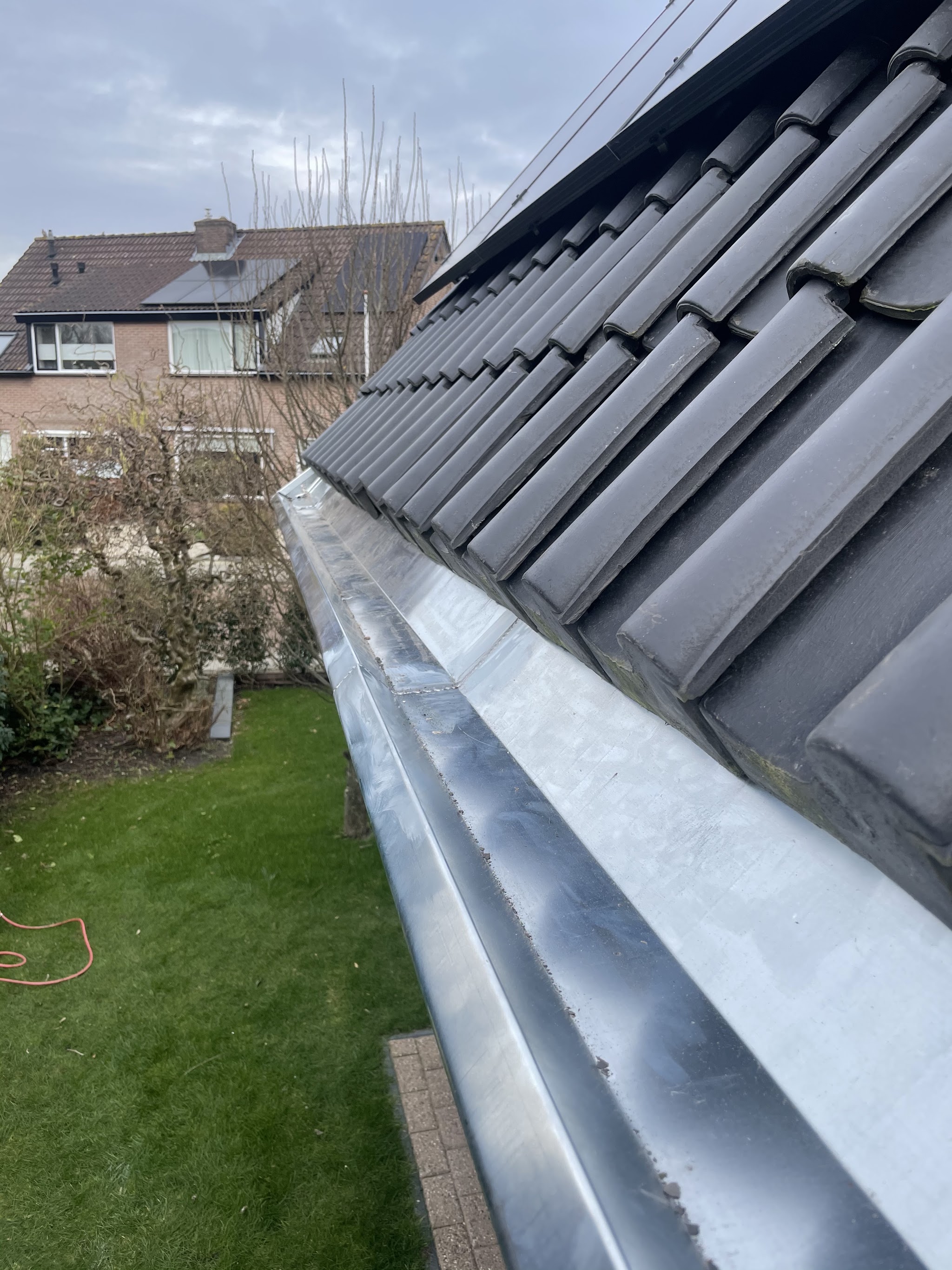 Nieuwe zinken mastgoot langs grijze dakpannen